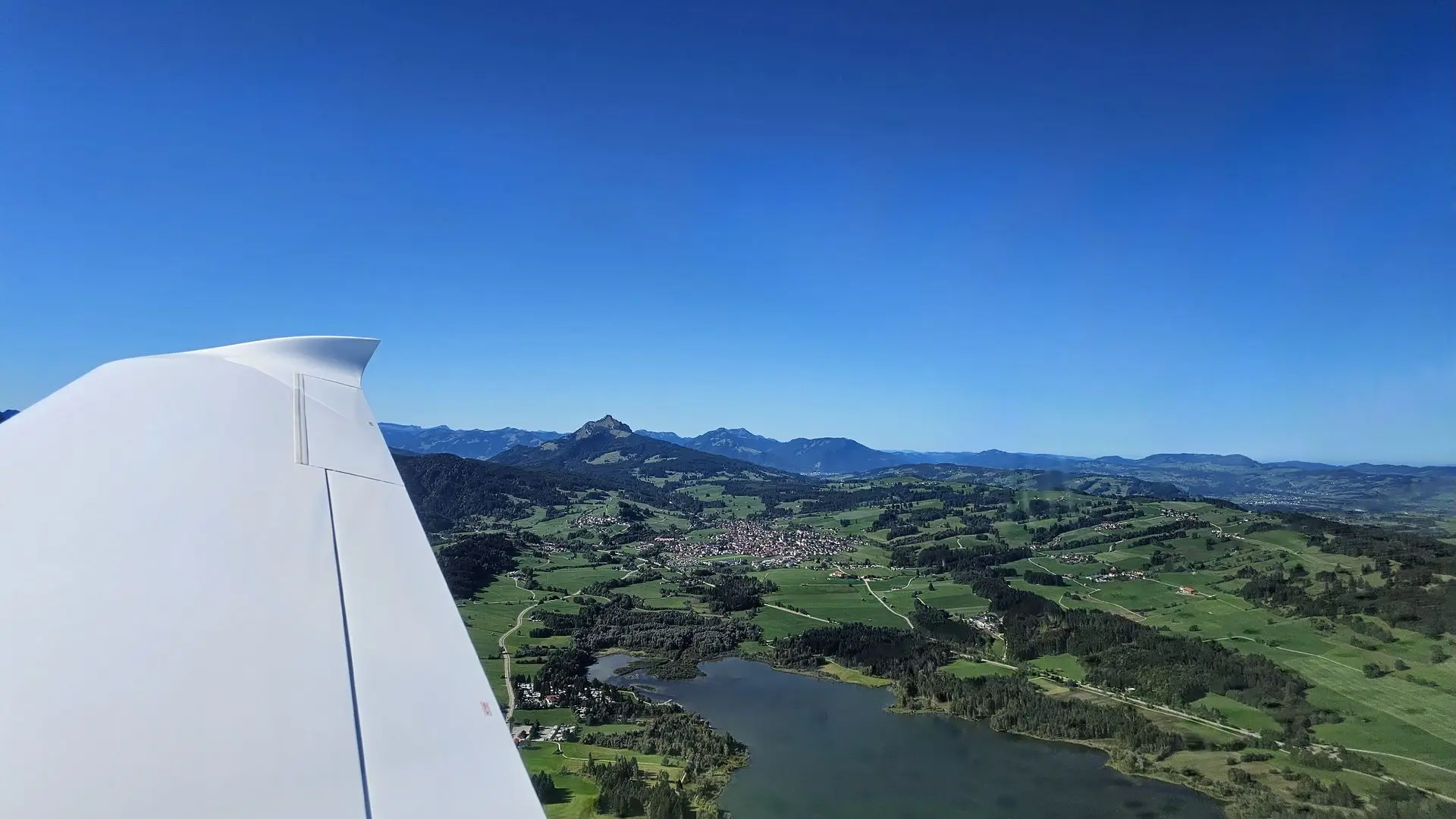 Vue depuis le cockpit : l’aile au-dessus d’un lac et des montagnes